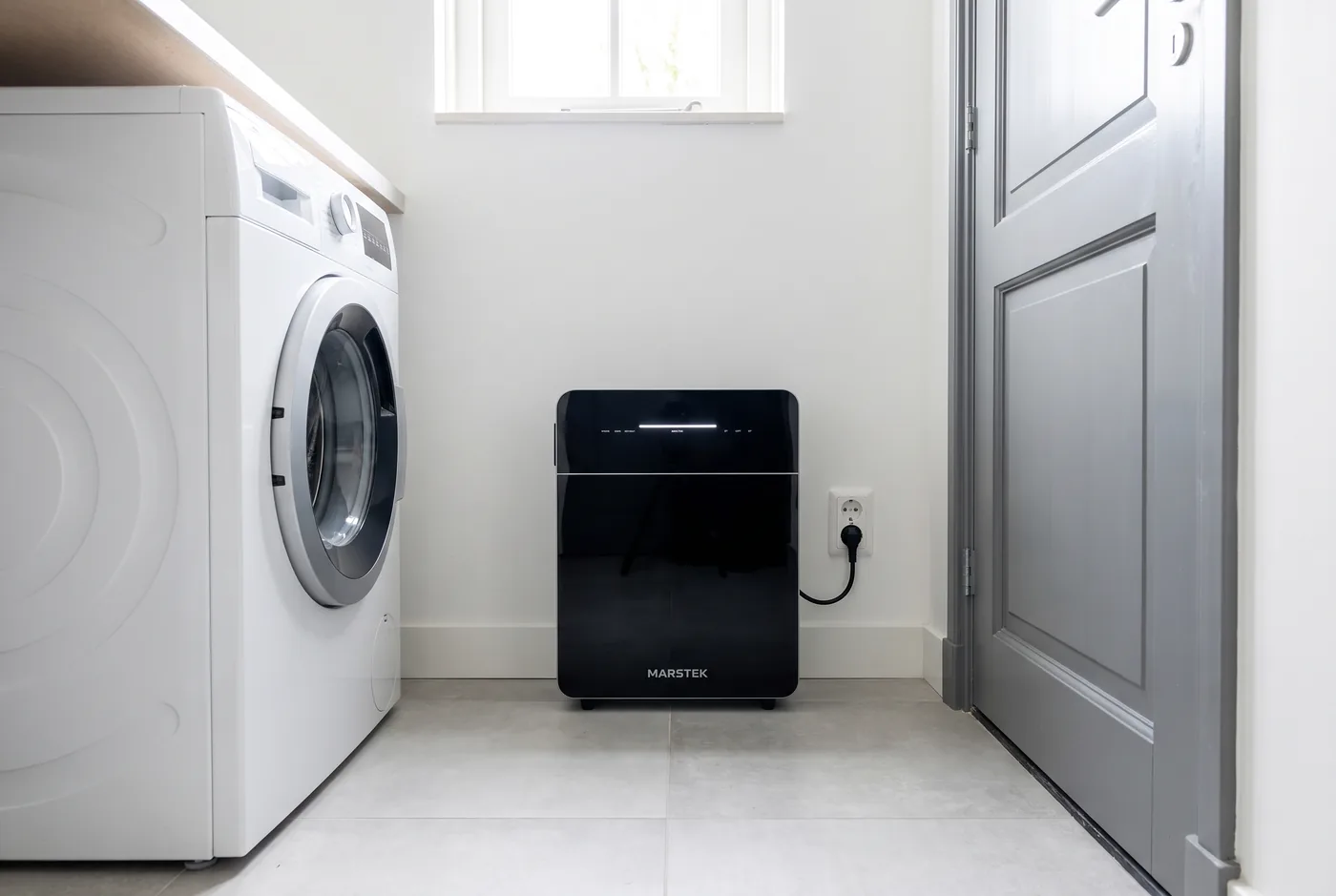 Marstek Venus E 3.0 in een bijkeuken naast de wasmachine, aangesloten op een stopcontact